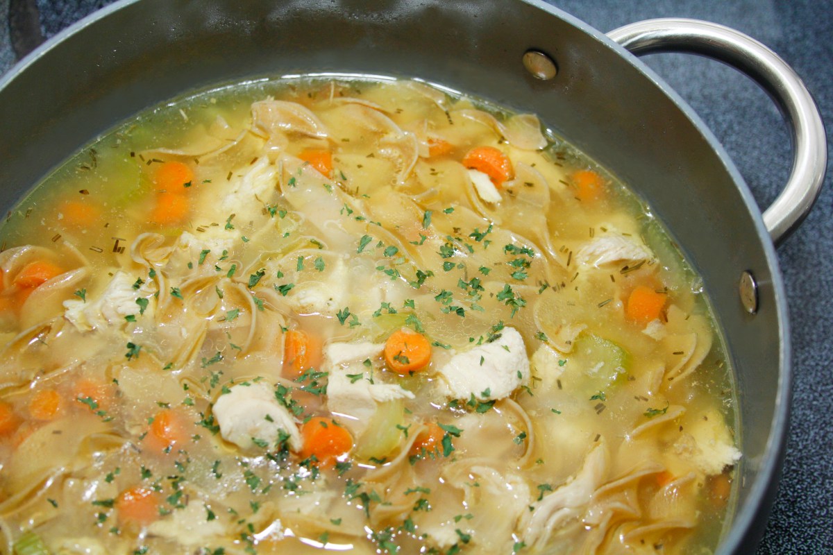 Homemade chicken noodle soup in a crockpot with carrots, celery, topped with parsley bits.