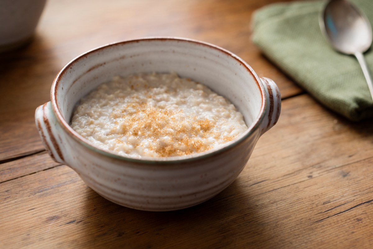 Photograph of a rustic hand made bowl filled with freshly made Porridge, topped with sprinkled Demerara sugar. Photographed on a rustic old pine rustic table.