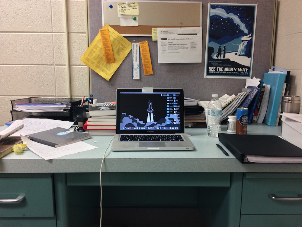 Karly: Desk on campus. Textbooks, notebooks, MacBook, several drinks (caffeine and non), Ibuprofen, some trash.