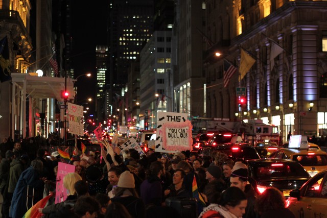 A large group of protesters holding signs on the sidewalk outside Trump Tower