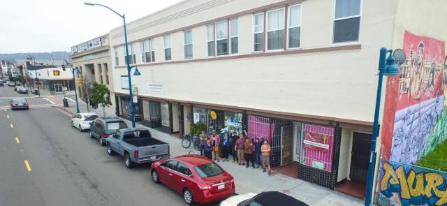 Photo of a group of people, shot from a distance and above, standing outside a building and waving at the camera