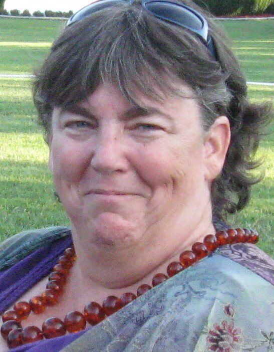 A white woman with short brown hair wearing a red plastic bead necklace smiles for the camera.