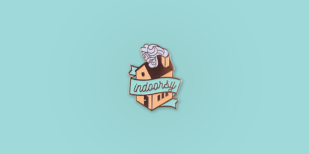 Indoorsy Enamel Pin / Description: House with swirly smoking chimney, banner across the front reads "Indoorsy" / Metal: Rose Gold / Enamel Colors: Coral and Mint