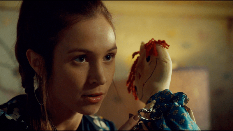 Waverly holds up a lighter and a creepy doll, ready to party