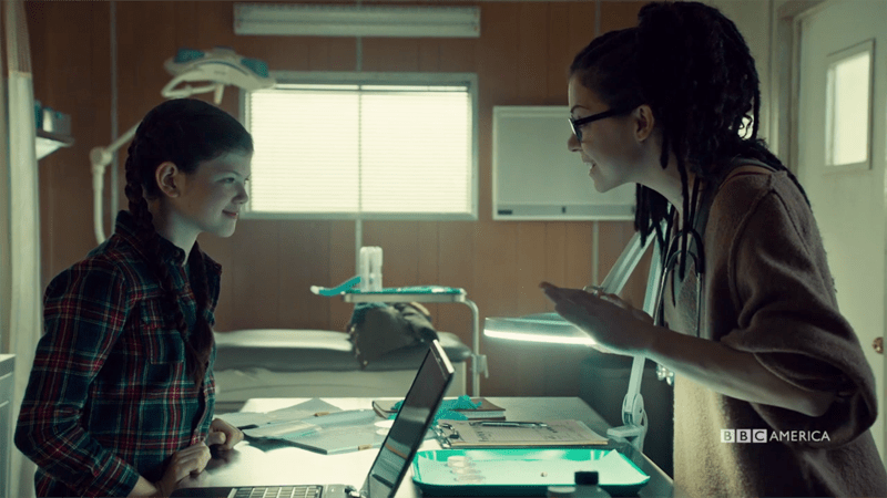 Cosima and Charlotte smile at.each other over a microscope 