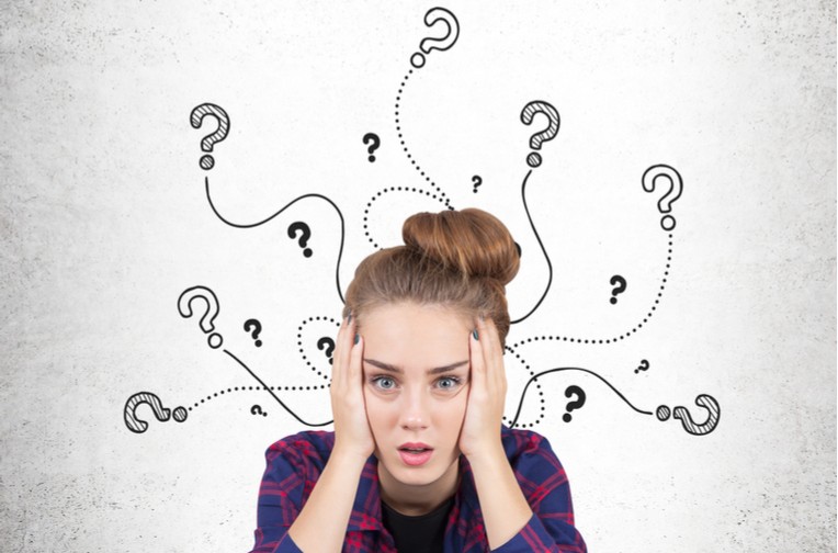 A young white woman in a flannel sits with her head in her hands as question marks swirl around her head.