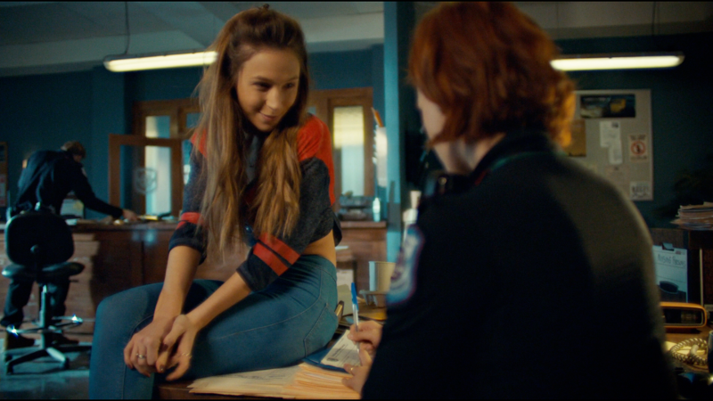 Waverly sits on Nicole's desk and smiles at her