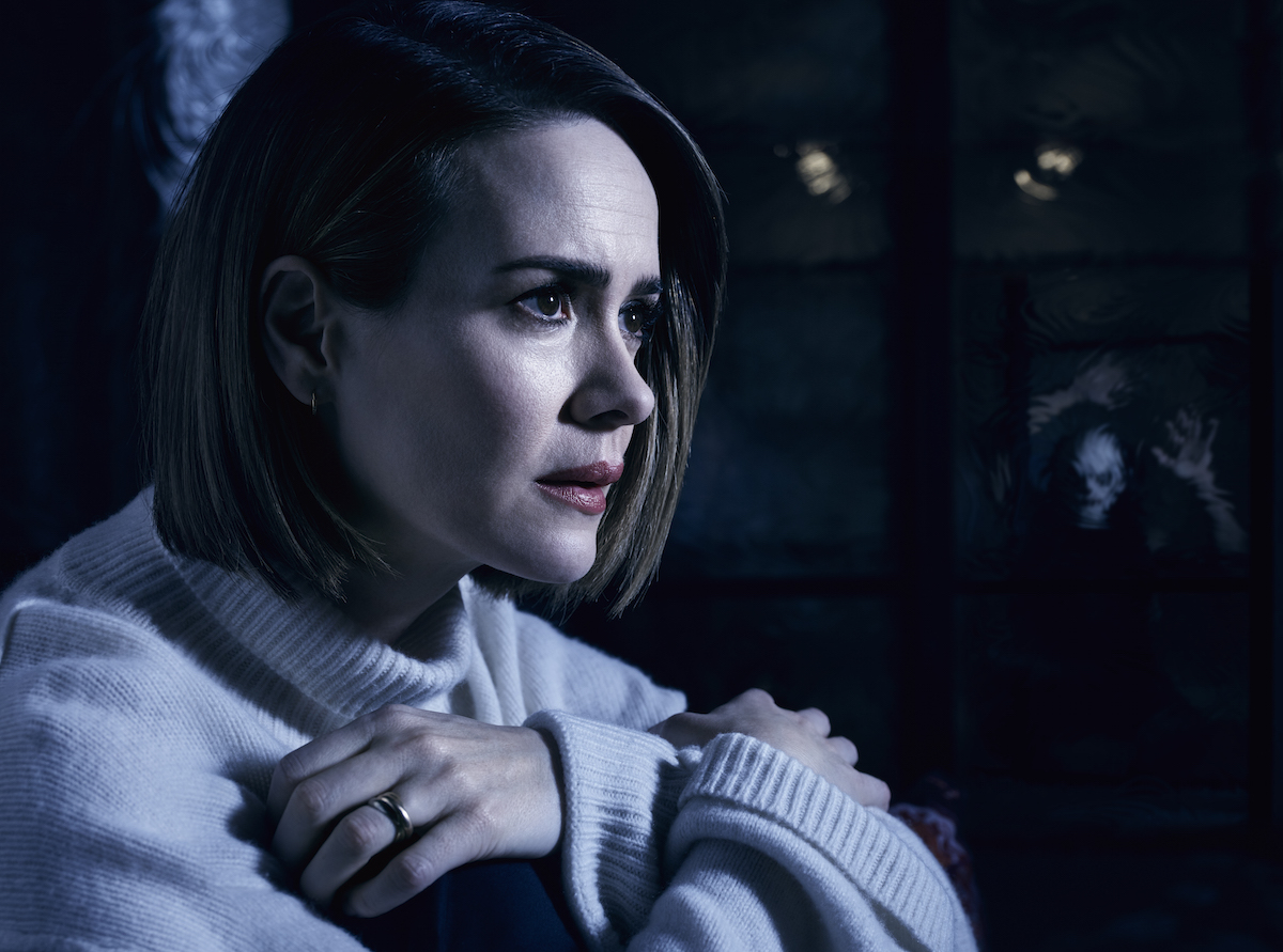Sarah Paulson in a tasteful mock turtleneck, clutching at her chest with a concerned expression