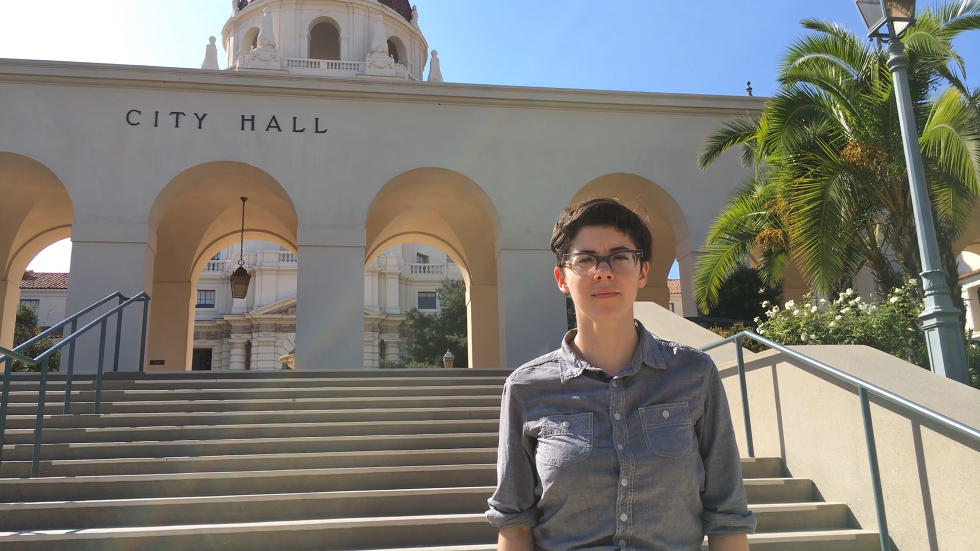 Carrie looks sternly into the camera in front of a City Hall building.