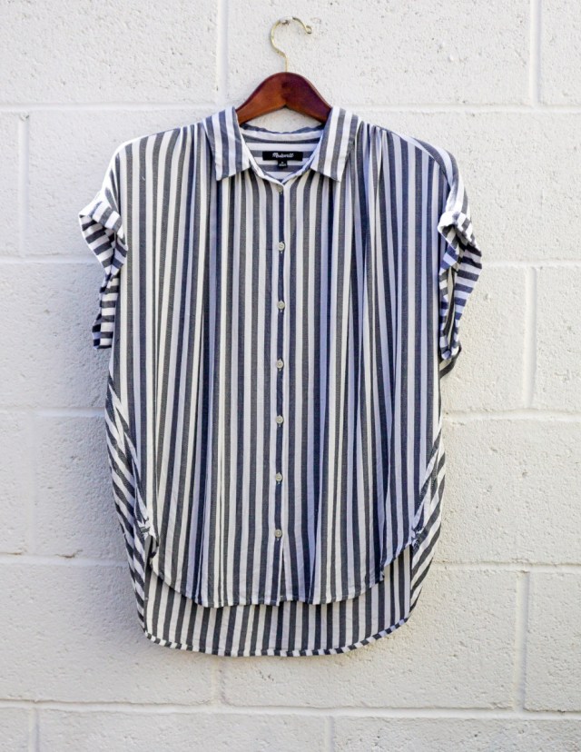 A blue and white striped shirt with short sleeves, hanging against a white brick wall.