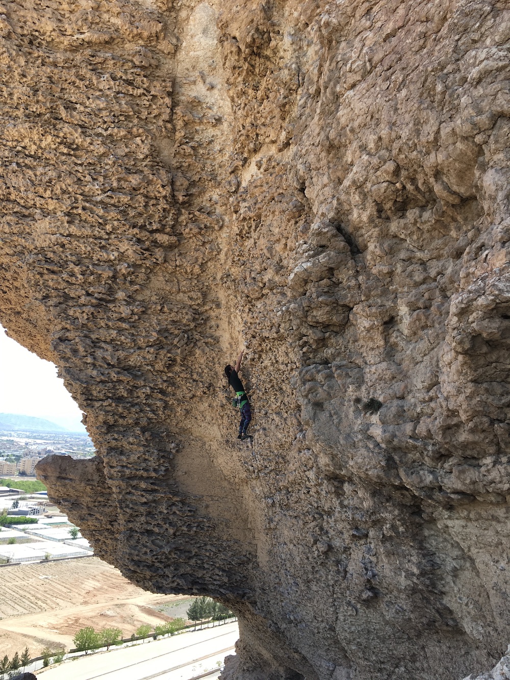 photo of the author climbing up a sheer rock face with a city in the background