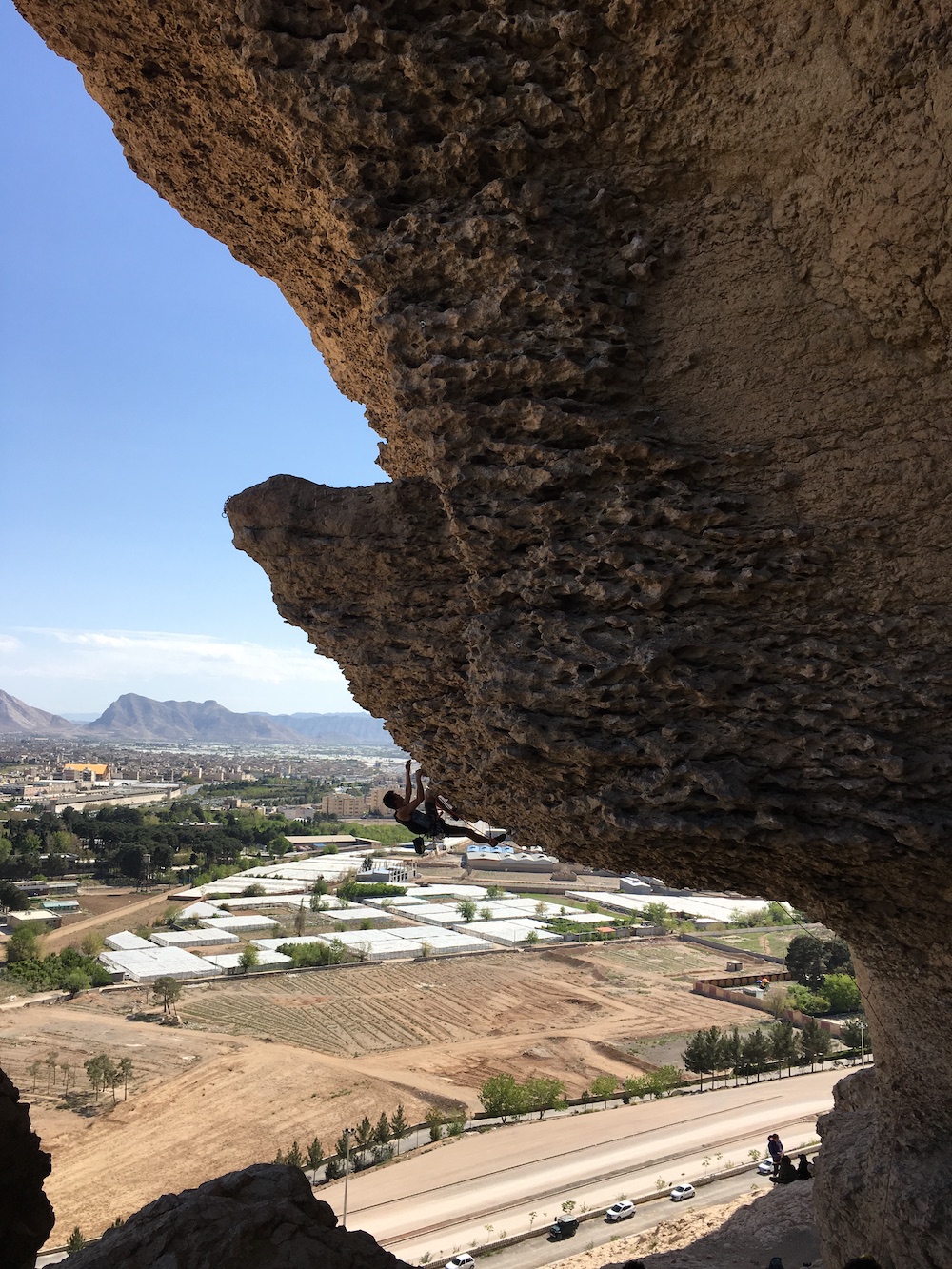 photo of someone climbing up a rock face, suspended on the underside of an outcropping