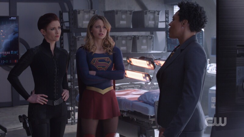 Alex stands with her hands on her hips, Supergirl with her arms crossed