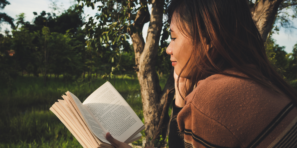 A femme person reading a paper book outside.