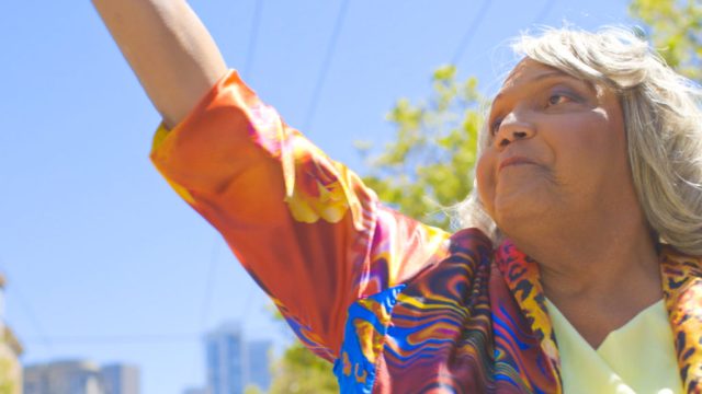 A recent photo of Miss Major raising her fist in power in the air.