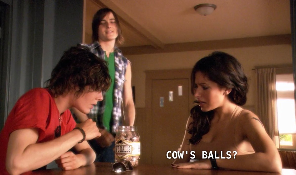 Shane and Carmen sit at the kitchen table inside Shane's house. Max stands next to them. Max has just given Shane and Carmen a present, a jar that is labeled "Cow's Balls". Max takes a ball out of the jar and pops it into his mouth, as Carmen asks skeptically, "Cow's Balls?"