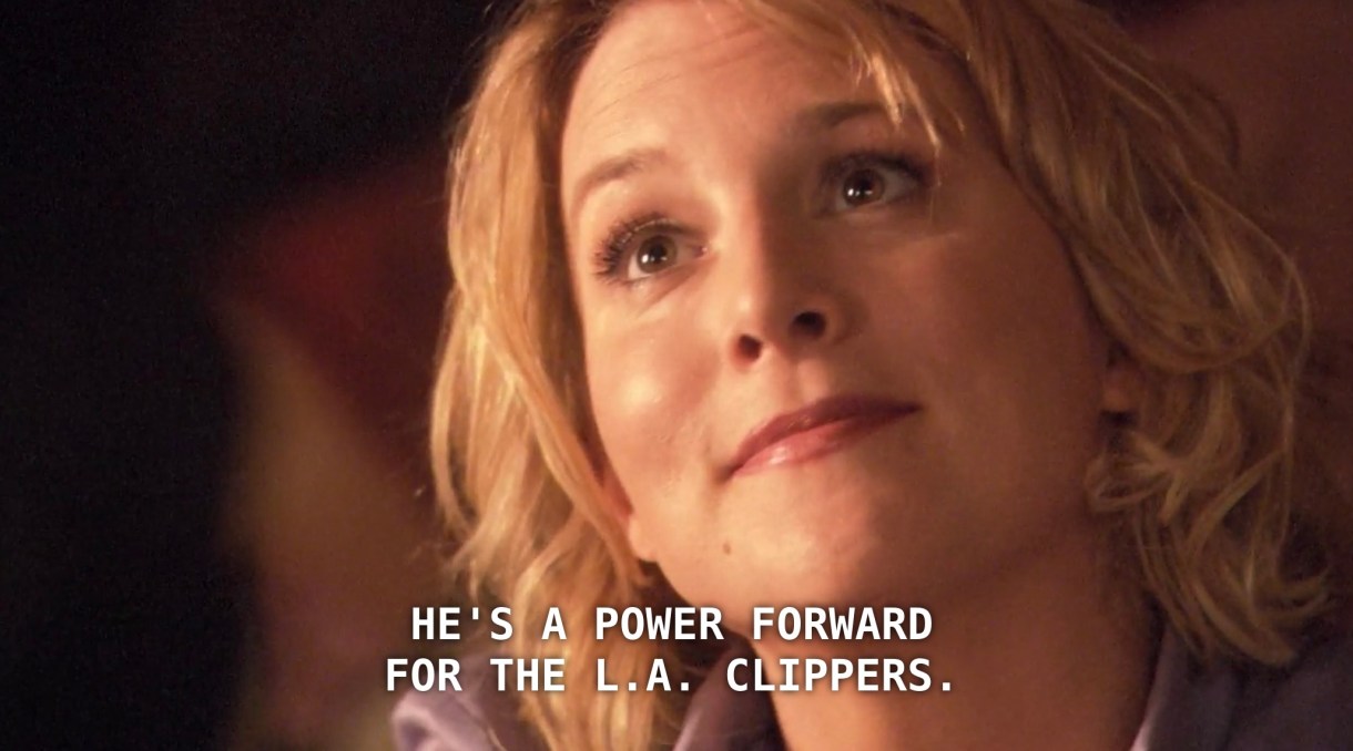 Tina, wearing a purple blouse and her hair in curls, looks up at a new client, who has just asked her what her husband does for work. Tina says, "He's a power forward for the L.A. Clippers."