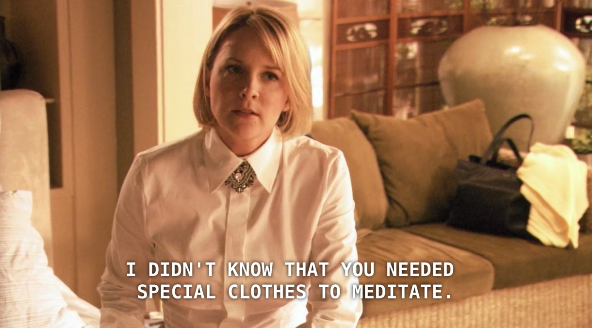 Tina (with straight blonde hair and a white shirt buttoned up all the way) sits in her house. She says to Bette, "I didn't know that you needed special clothes to meditate."