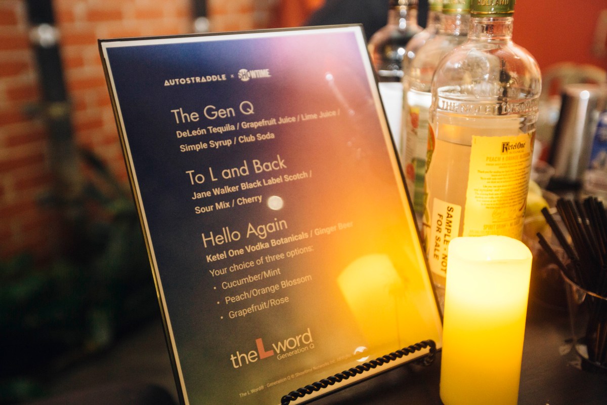 A photo of the drink menu with L Word-themed drinks, propped up next to a lit candle and bottles of liquor. 