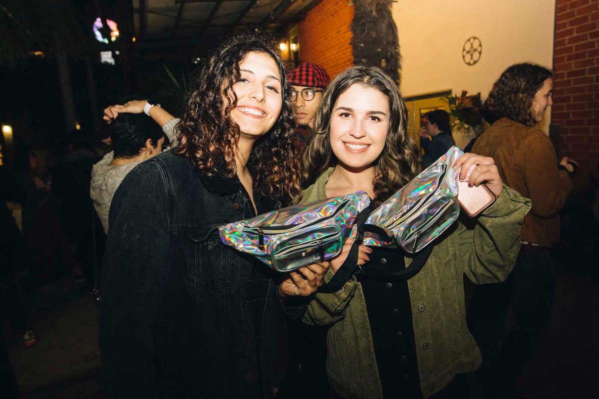 Two people posing with their silver sparkly fanny packs from the merch table. They are both smiling.