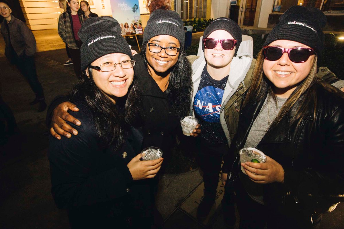 A group of four people holding drinks and posing for a picture with their arms around each other.