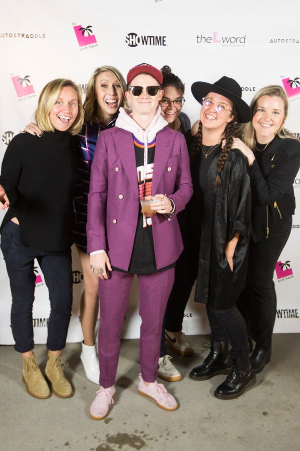 A group of 6 people all huddled together in front of a promo poster for "The L Word: Generation Q."