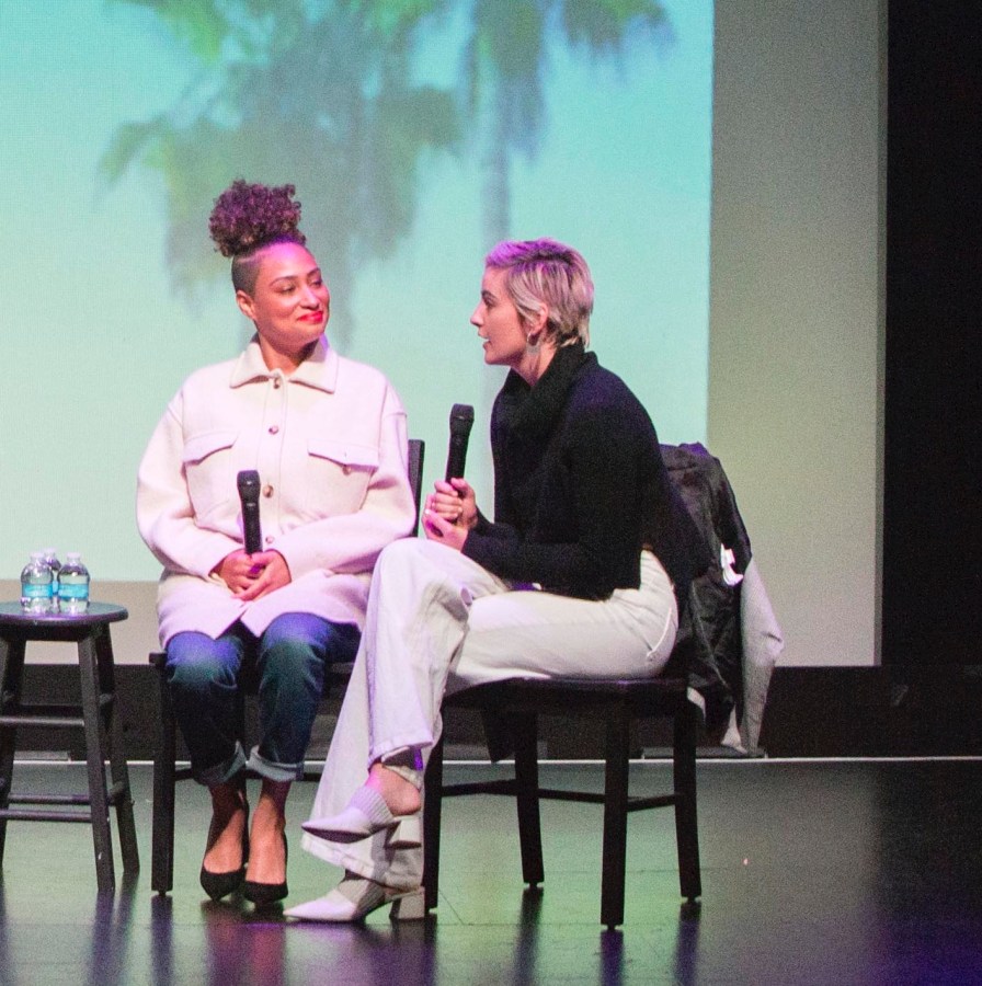 Rosanny Zayas (Sophie) and Jacqueline Toboni (Finley) sit next to each other on stage. Jacqueline is speaking into a microphone while Rosanny looks at her and smiles.