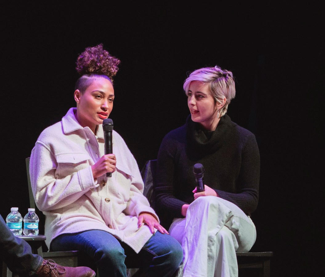 Rosanny Zayas and Jacqueline Toboni sit next to each other on stage. Rosanny is speaking into the microphone and Jacqueline is looking at her and listening intently.