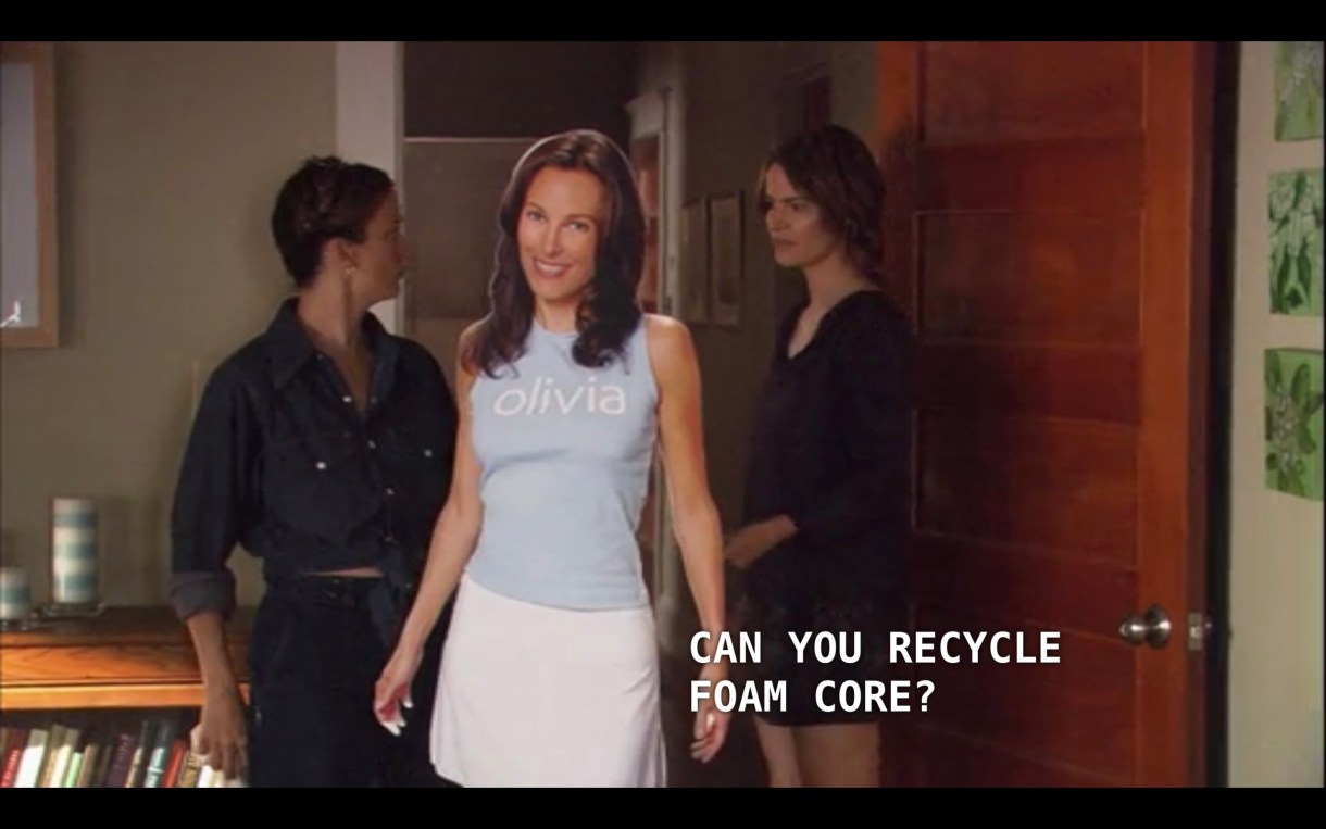 Alice (wearing a short black dress) stands in the doorway of her apartment with a house cleaner (a woman wearing a long chambray shirt and her hair braided). The lifesize cutout of Dana is in between them. Alice asks, "Can you recycle foam core?"