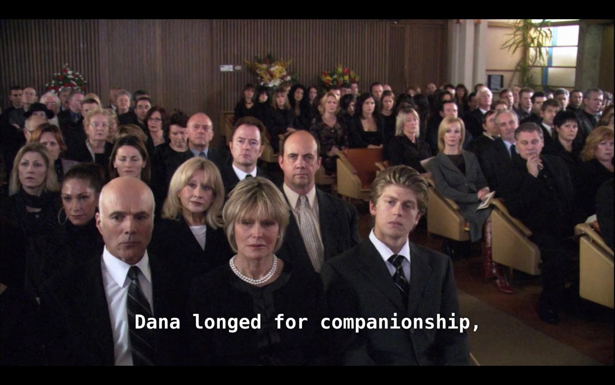 A crowd of people dressed in all black attending Dana's funeral service. The minister (off camera) says, "Dana longed for companionship."