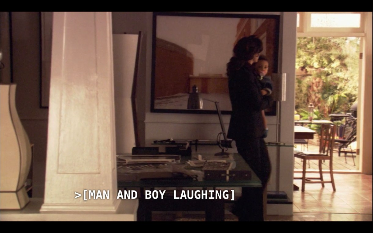 Bette (wearing a black pantsuit) is carrying Angelica through her house. The subtitles say, "[Man and boy laughing]"