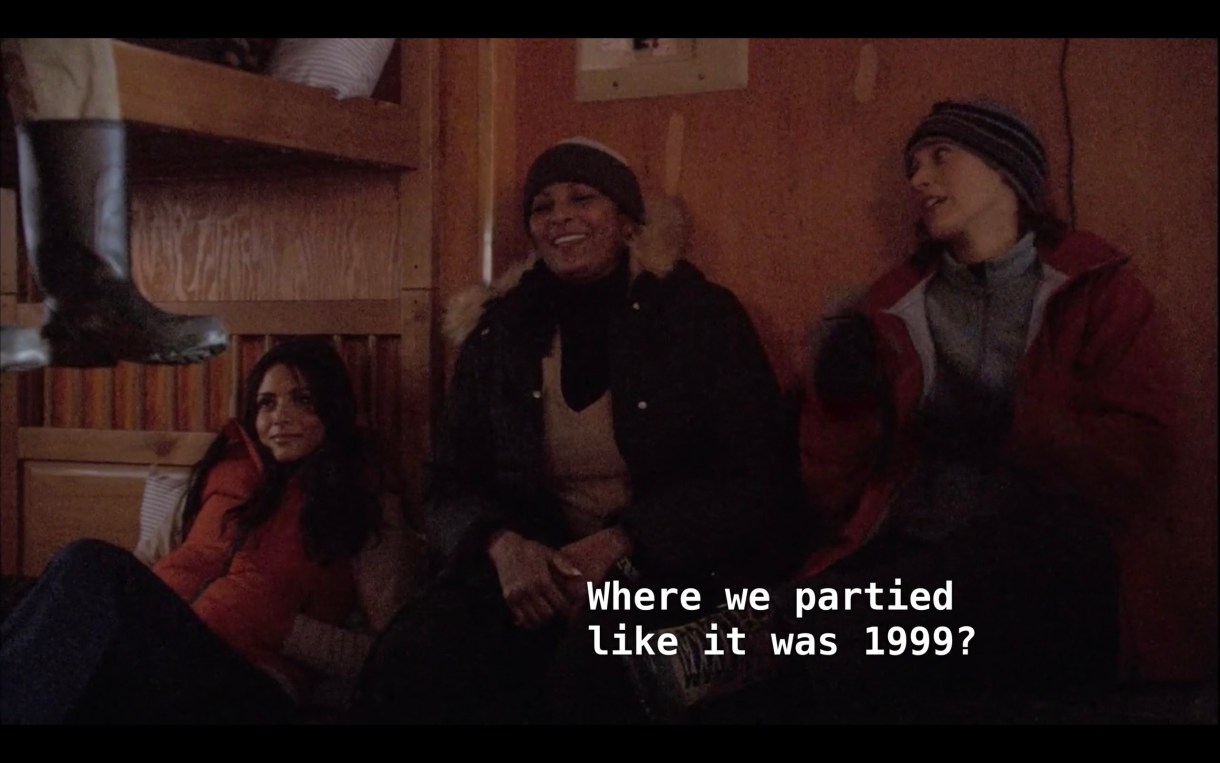 Carmen (wearing an orange puffy vest), Kit (wearing a fur lined black jacket), and Bette (wearing a red jacket) sit next to each other in a cabin. Kit asks, "Where we partied like it was 1999?"