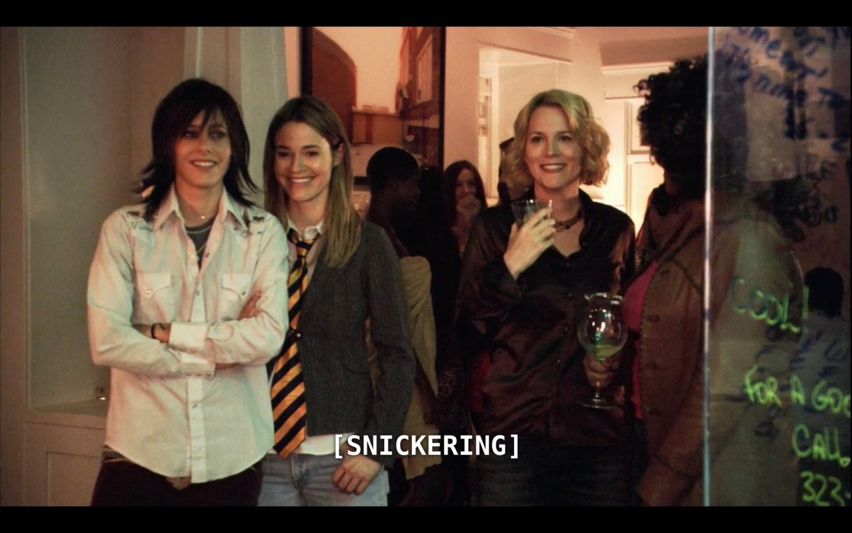 A flashback scene in which Shane (wearing a white button-up), Alice (wearing a grey sweater and black-and-yellow striped neck tie) and Tina (wearing a dark brown blouse and holding a cocktail glass) are standing at a party. The subtitles say, "[Snickering]"