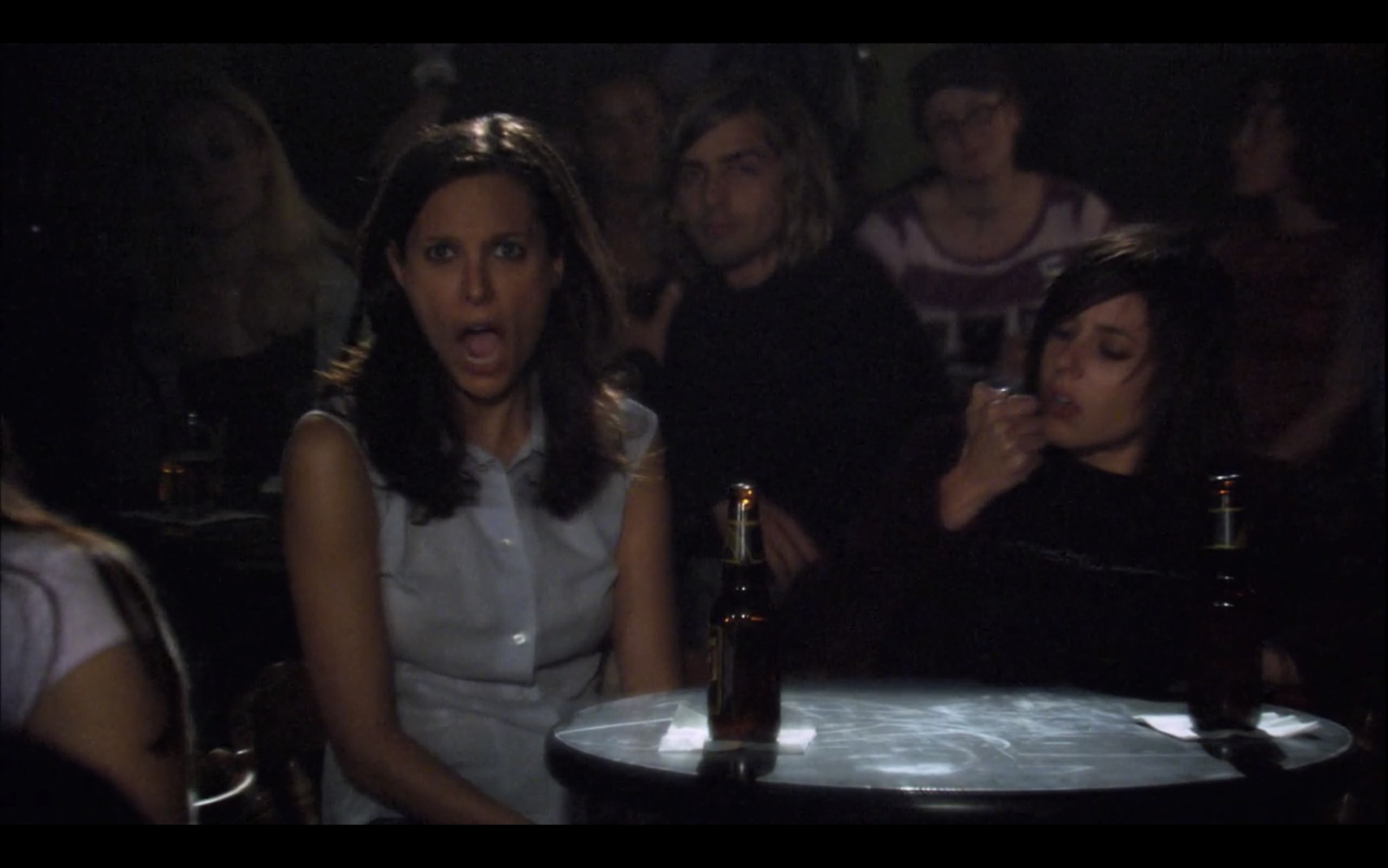 Dana and Shane sit at a table at a crowded Tegan and Sara concert. Dana's jaw has dropped, while Shane inspects her fingernail.