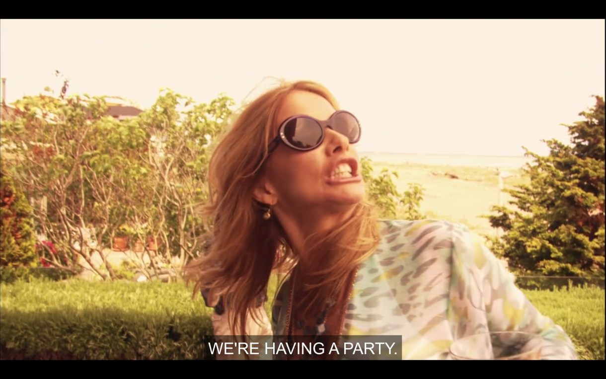 Cherie screams "WE'RE HAVING A PARTY." She's wearing sunglasses, the beach is behind her, she looks bananas