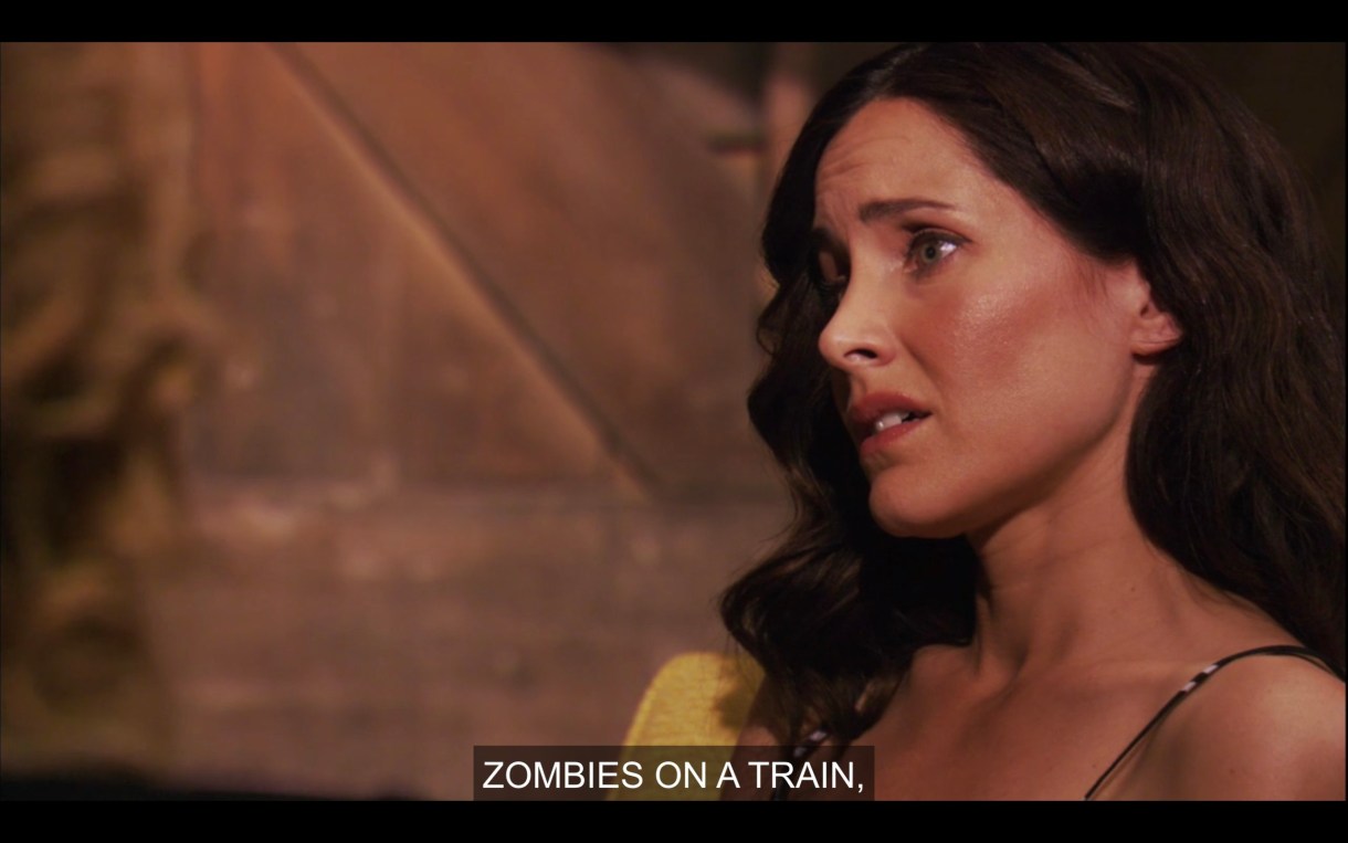 Helena sits in a yellow chair, looking disappointed after getting fired. Tina, who is off screen, says "Zombies on a Train."