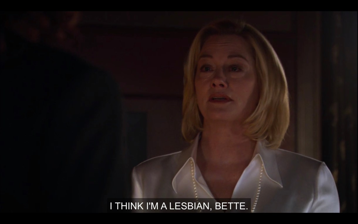 Phyllis is wearing a white silk blouse and a long strand of pearls. She says, "I think I'm a lesbian, Bette."