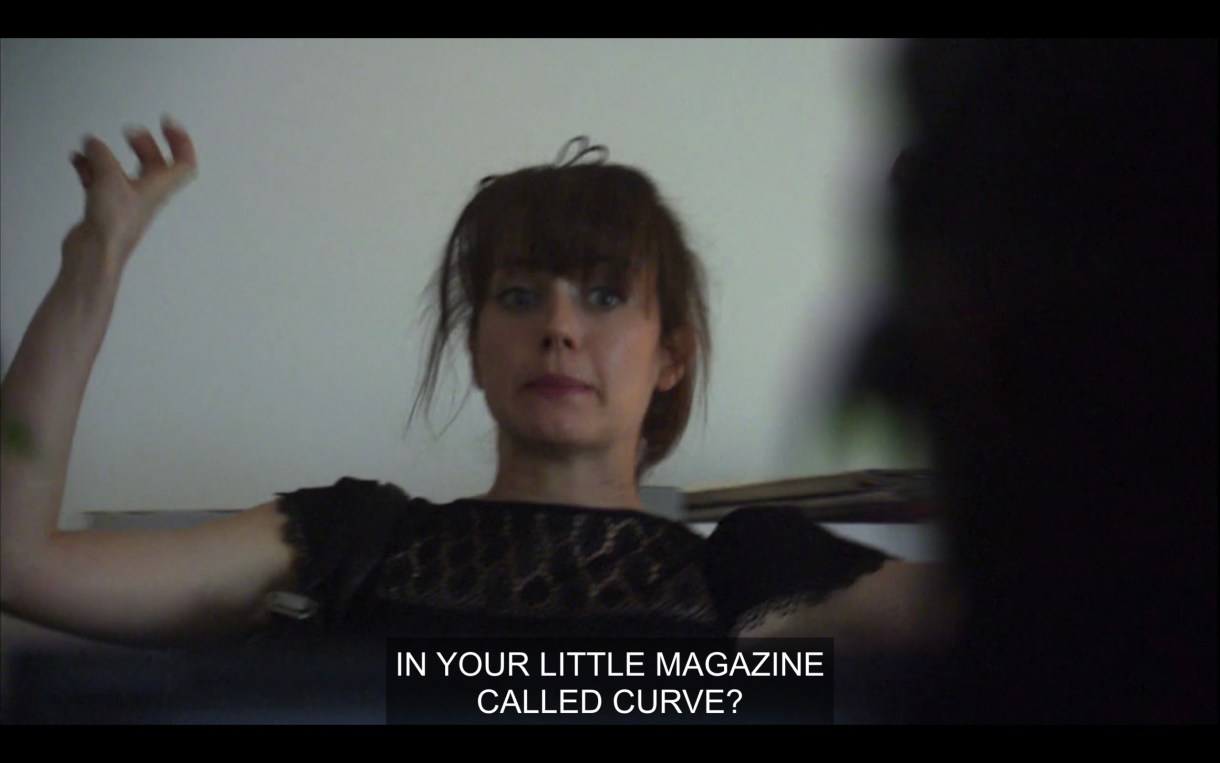 Jenny is sitting back in a chair with her arms in the air. She says, "In your little magazine called Curve?"