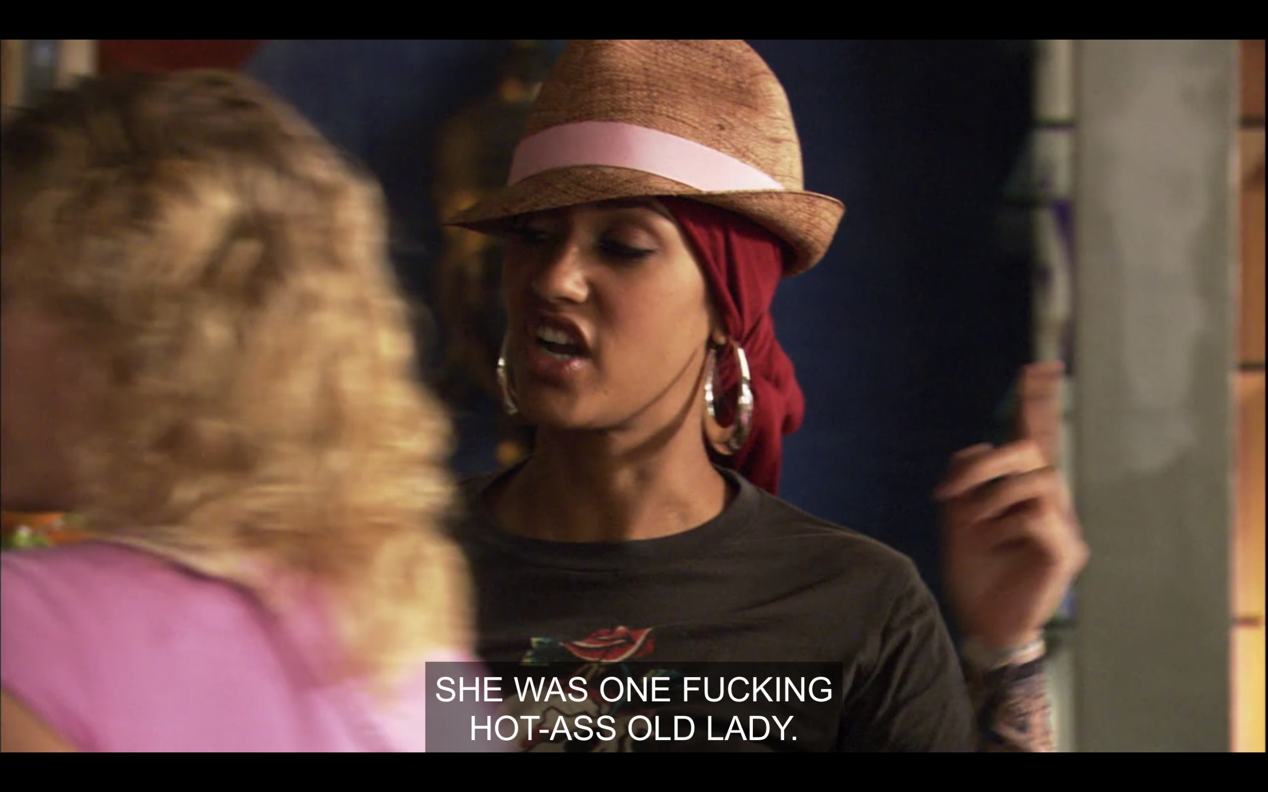 Papi is wearing a fedora and hoop earrings. She says, "She was one fucking hot-ass old lady."