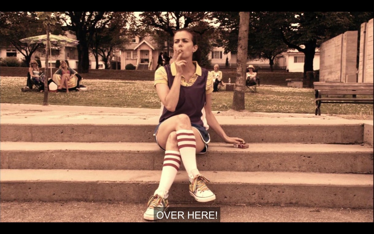 Jenny sitting on some concrete steps with her legs crossed, smoking a cigarette.