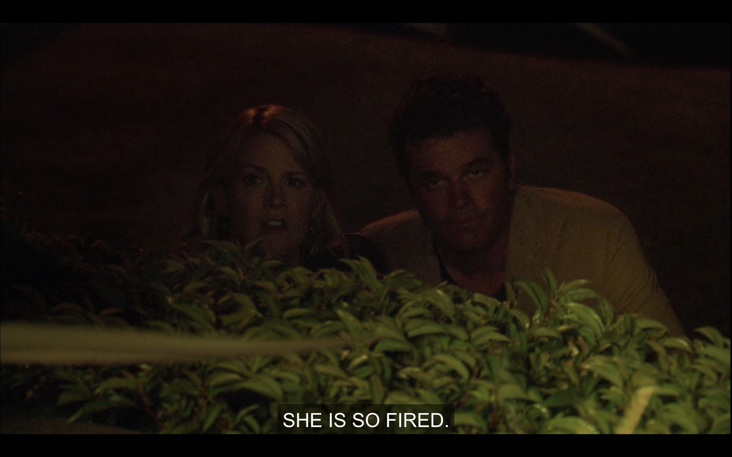 Tina and Henry hiding behind a bush in the dark. Tina says, "She is so fired."