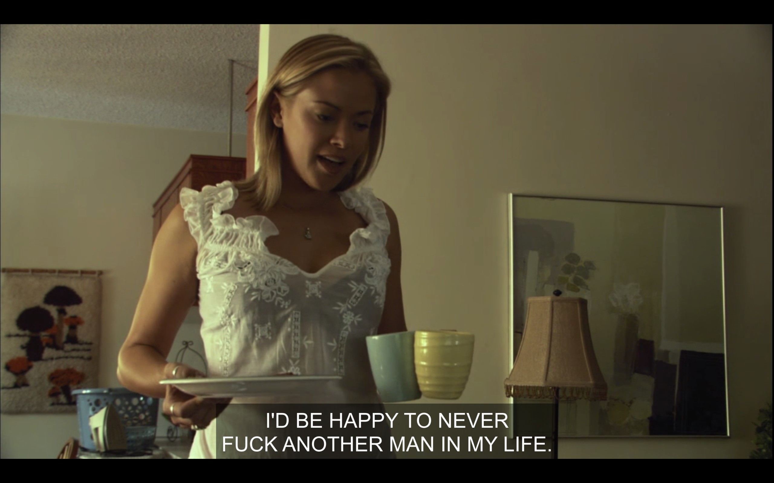 Paige (wearing a white blouse) holds a plate and two coffee mugs in her hands. She says, "I'd be happy to never fuck another man in my life." 