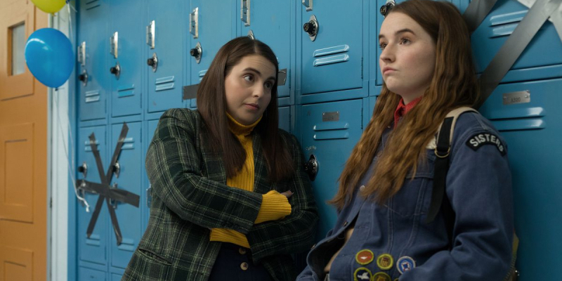 Two teen girls lean on blue lockers.