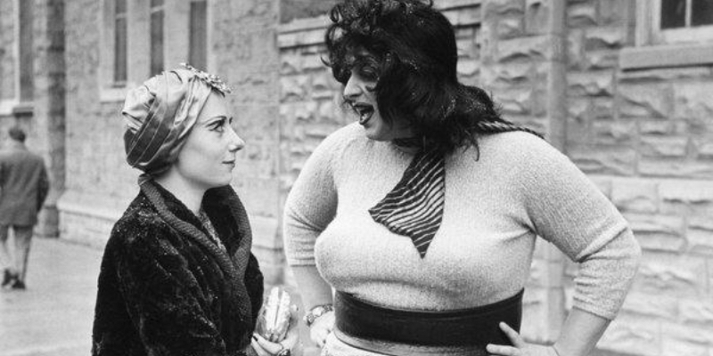 Divine talks to Mink Stole with her arms on her waist. 
