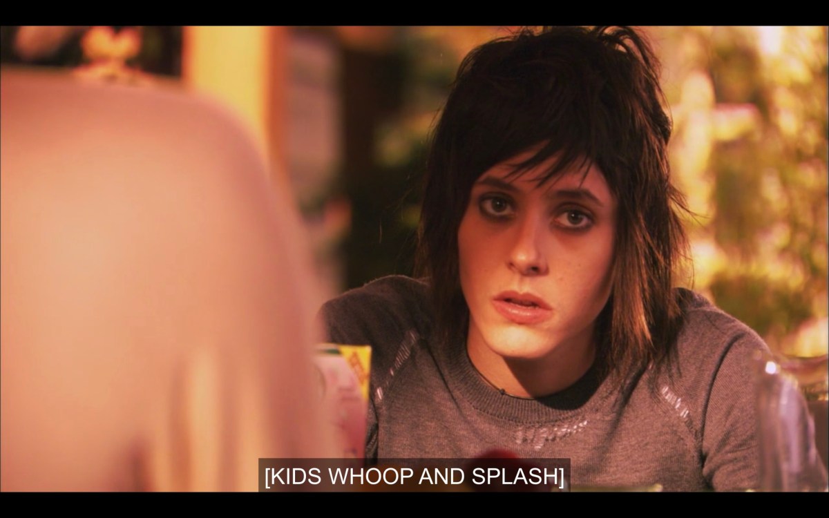 Shane in a grey t-shirt, looking very tired, her black eyeliner smudged. Subtitles read, "[Kids whoop and splash]"