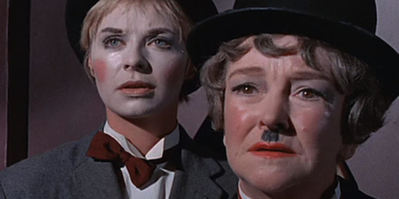 A sad woman dressed as Charlie Chaplin stands in front of a younger woman with mime makeup. 