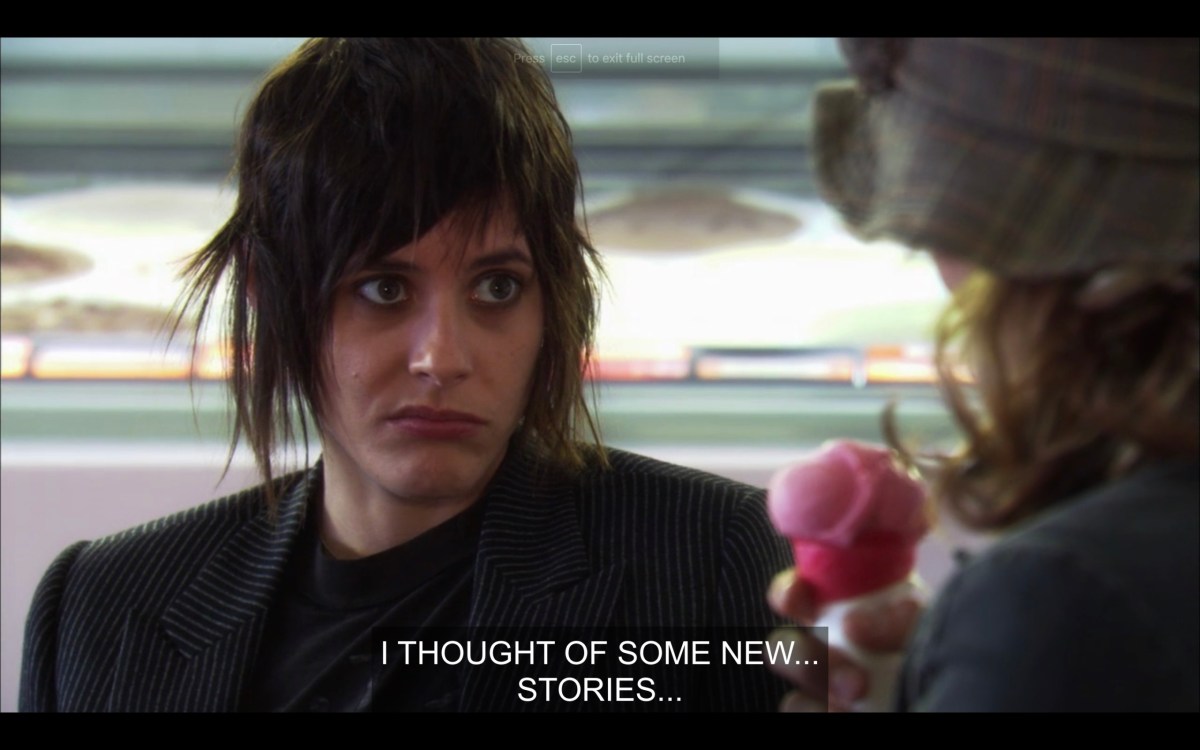 Shane (wearing a black jacket) and Paige (whose back is to the camera, and is holding a strawberry ice cream cone) sit in a coffee shop. Shane has a look of dislike on her face. Paige says, "I thought of some new... stories..." 