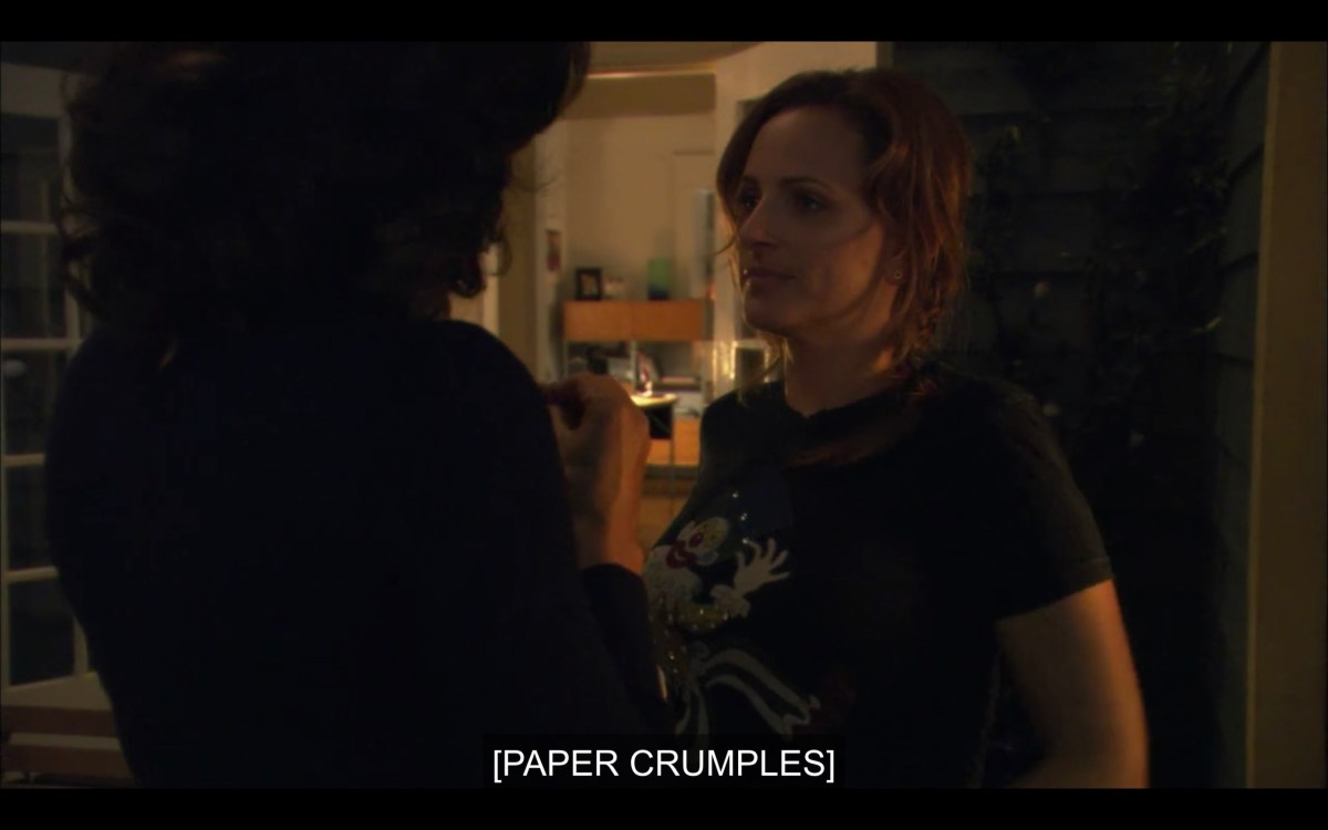 Jodi and Bette (whose back is to the camera) in Bette's house. Subtitles read "[Paper crumples]"