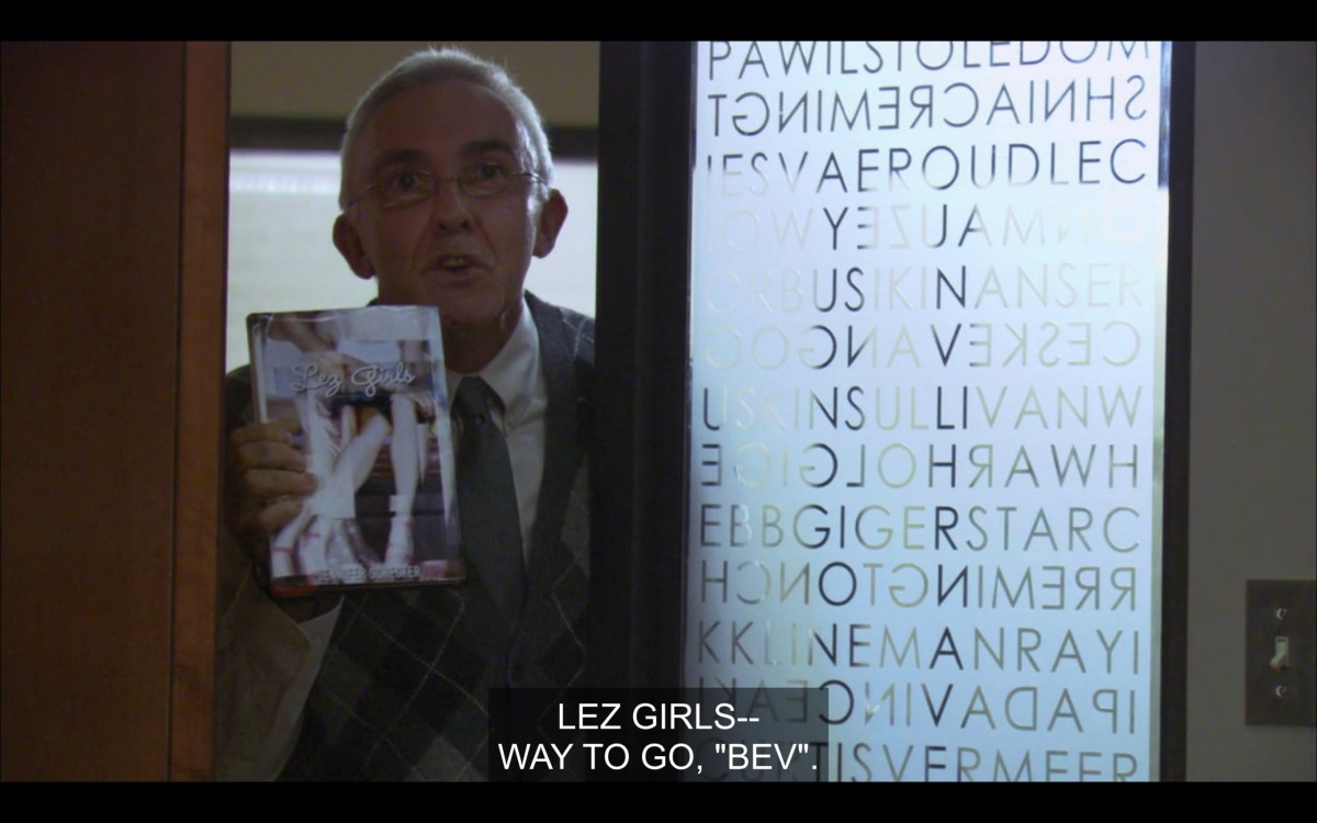 An old guy in a full suit and tiny glasses holds a copy of Les Girls up to the window looking into Bette's office. He says, "Lez Girls -- Way to go, 'Bev.'"