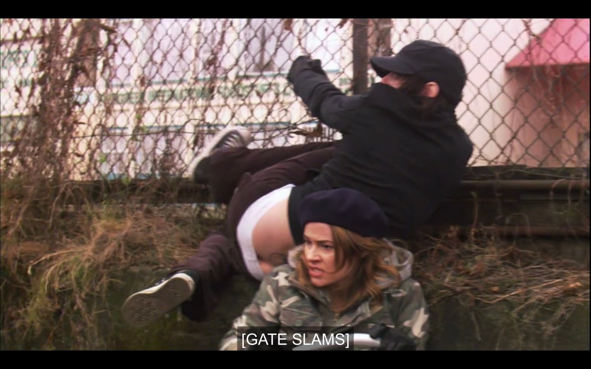 Alice (wearing a black beret and an camouflage jacket) and Shane (wearing all black, her pants falling down slightly) have just hopped a chain link fence and are now on the ground. Subtitles read, "[Gate slams]"